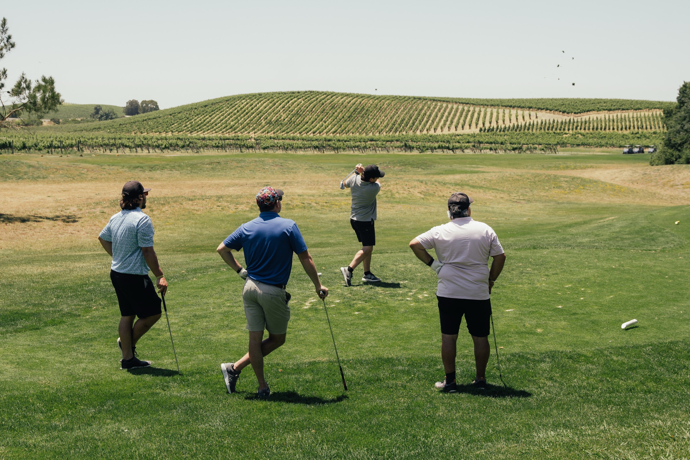 A foursome watches a drive at the Tee Off Fore Kids tournament, Napa vineyard hills behind